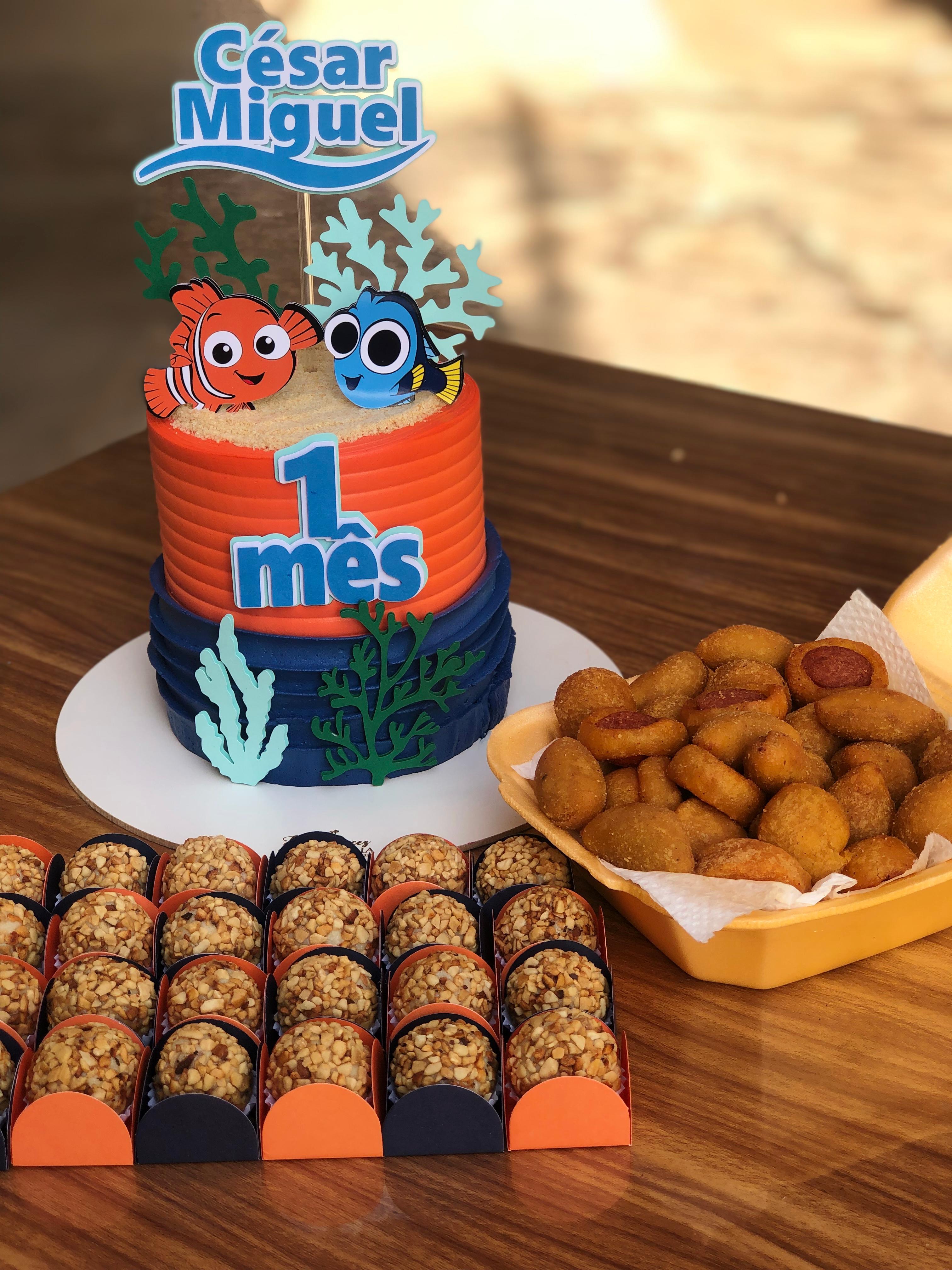 Bolo azul com topper infantil ao lado de docinhos e salgados
