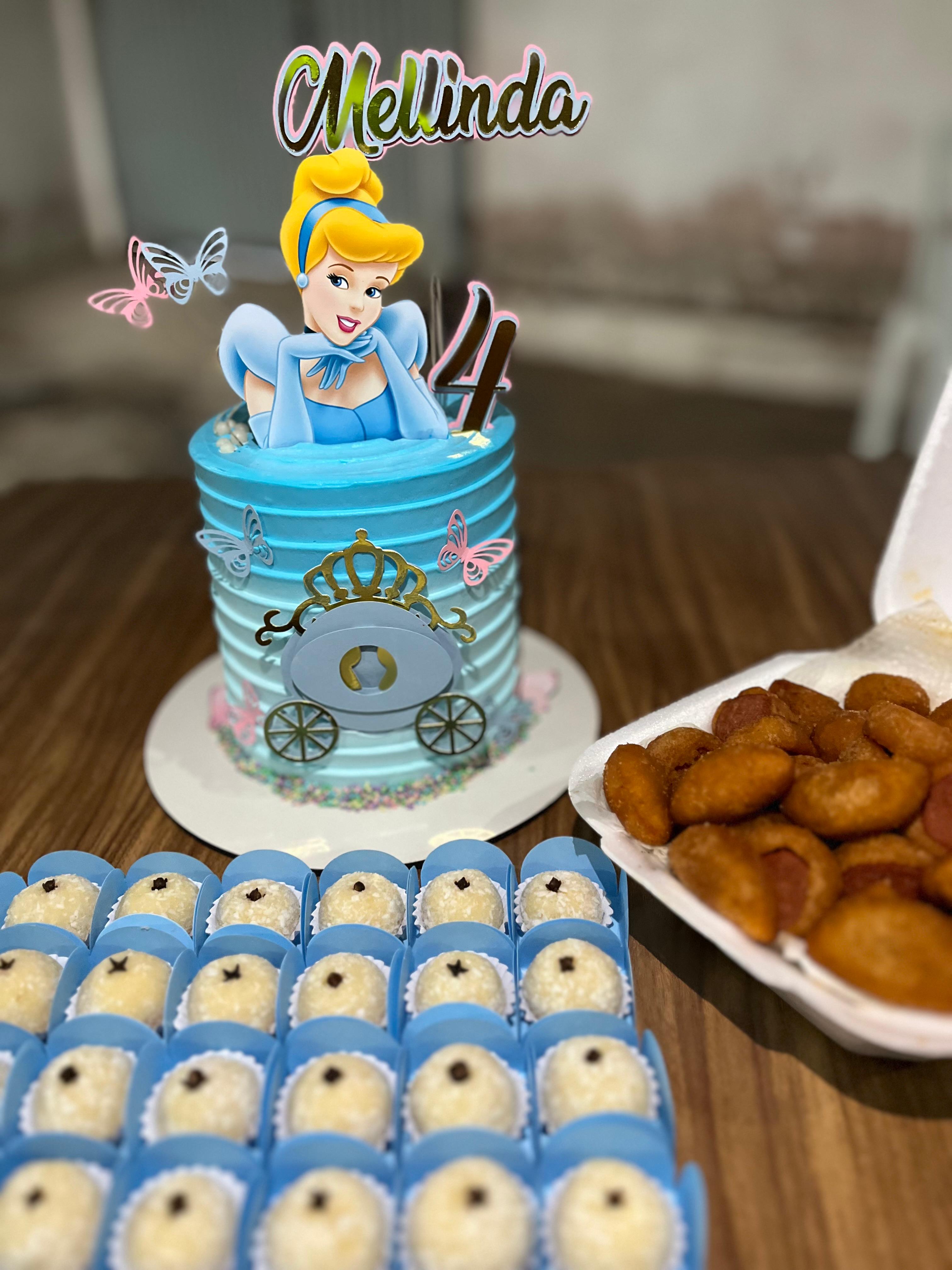 Bolo azul com personagem de princesa, docinhos decorados e salgados ao lado